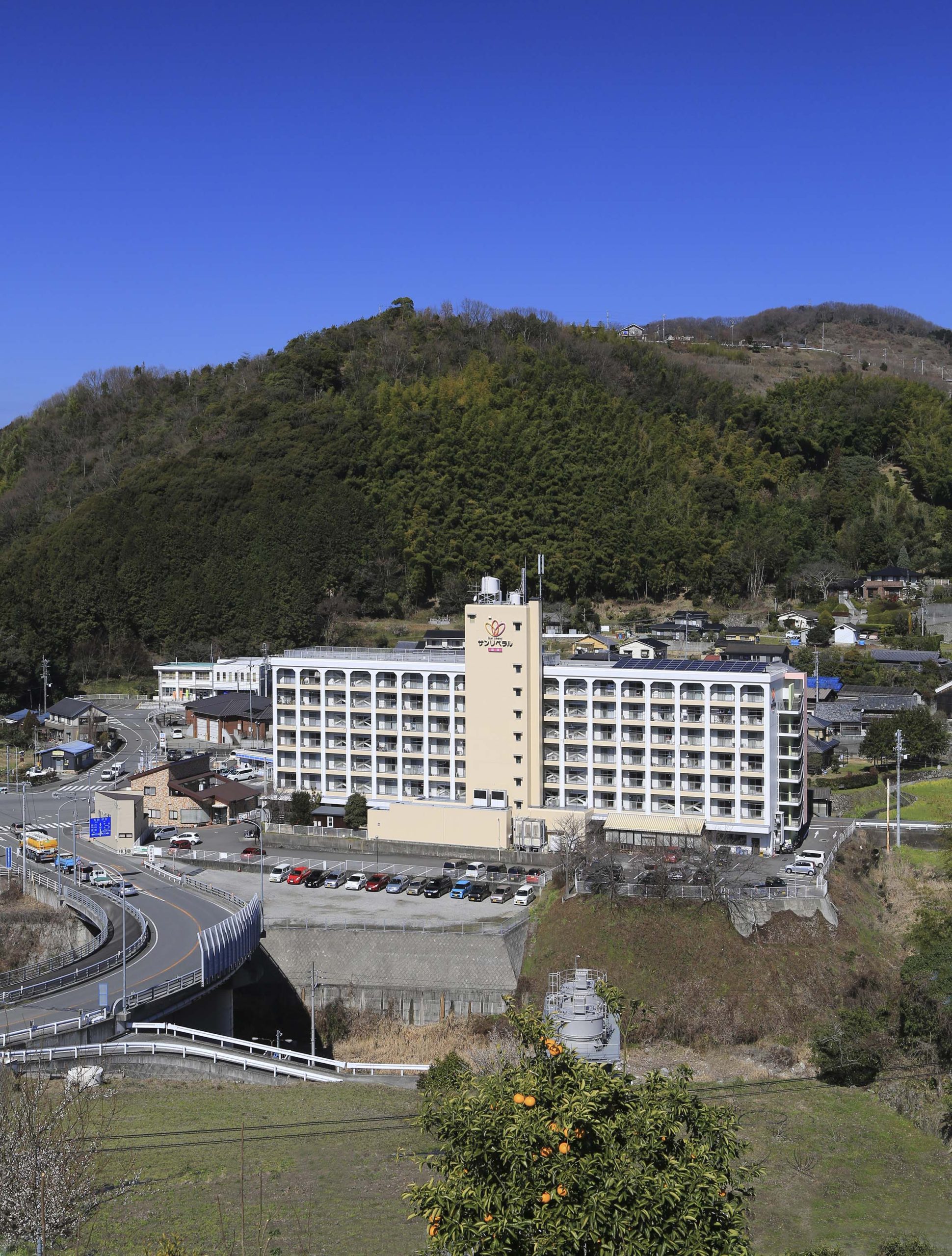 丘陵地に立地する多層白色介護施設の外観。駐車場と周辺環境を含む全景